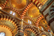 Mehrfarbig marmorierte Mauern, Wandmalereien und farbenfrohe Mosaike machen aus der Basilika Notre Dame de la Garde in Marseille, Frankreich, ein prächtiges Gesamtkunstwerk - © Curioso / Shutterstock