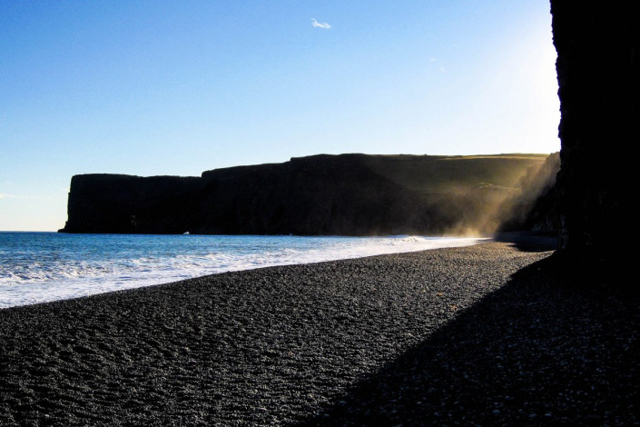 Kurz vor Sonnenuntergang schaffen die pechschwarzen Felsen in der Lagune Dyrhólaós mit dem Blau von Himmel und Meer einmalige Farbenspiele, Island
