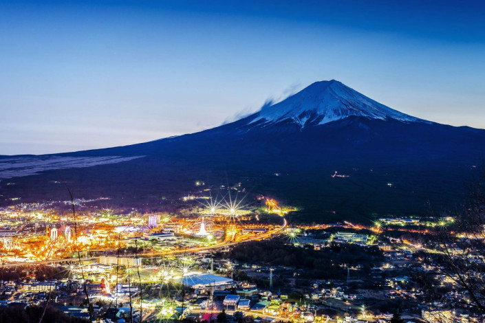 Die hell erleuchtete Stadt Fujiyoshida in der Dämmerung am Fuß des berühmten Mount Fuji in Japan