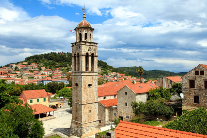 In einem Meer aus roten Ziegeldächern thront auf dem malerischen Hauptplatz von Blato die stolze Allerheiligen-Kirche Svih Svetih, Insel Korcula, Kroatien
