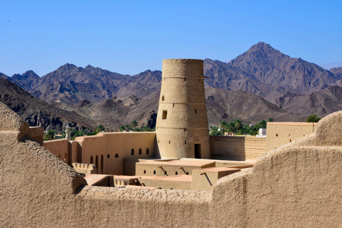 Die hellen, sandfarbenen Mauern der Festung von Bahla heben sich deutlich vor dem dunklen Hintergrund des gewaltigen Gebirgszuges Jebel Akhdar ab, Oman