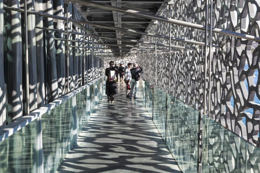 Bei Sonnenschein wirft das filigrane Betonnetz um das MuCEM in Marseille, Frankreich, Schattenspiele auf den dahinter liegenden Gang - © meinzahn / Shutterstock