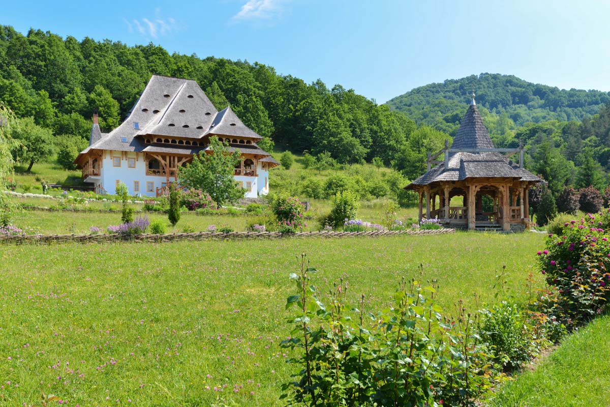Die Holzbauten der Klosteranlage von Bârsana, Rumänien, fügen sich in einen idyllischen Garten mit Blumenbeeten ein