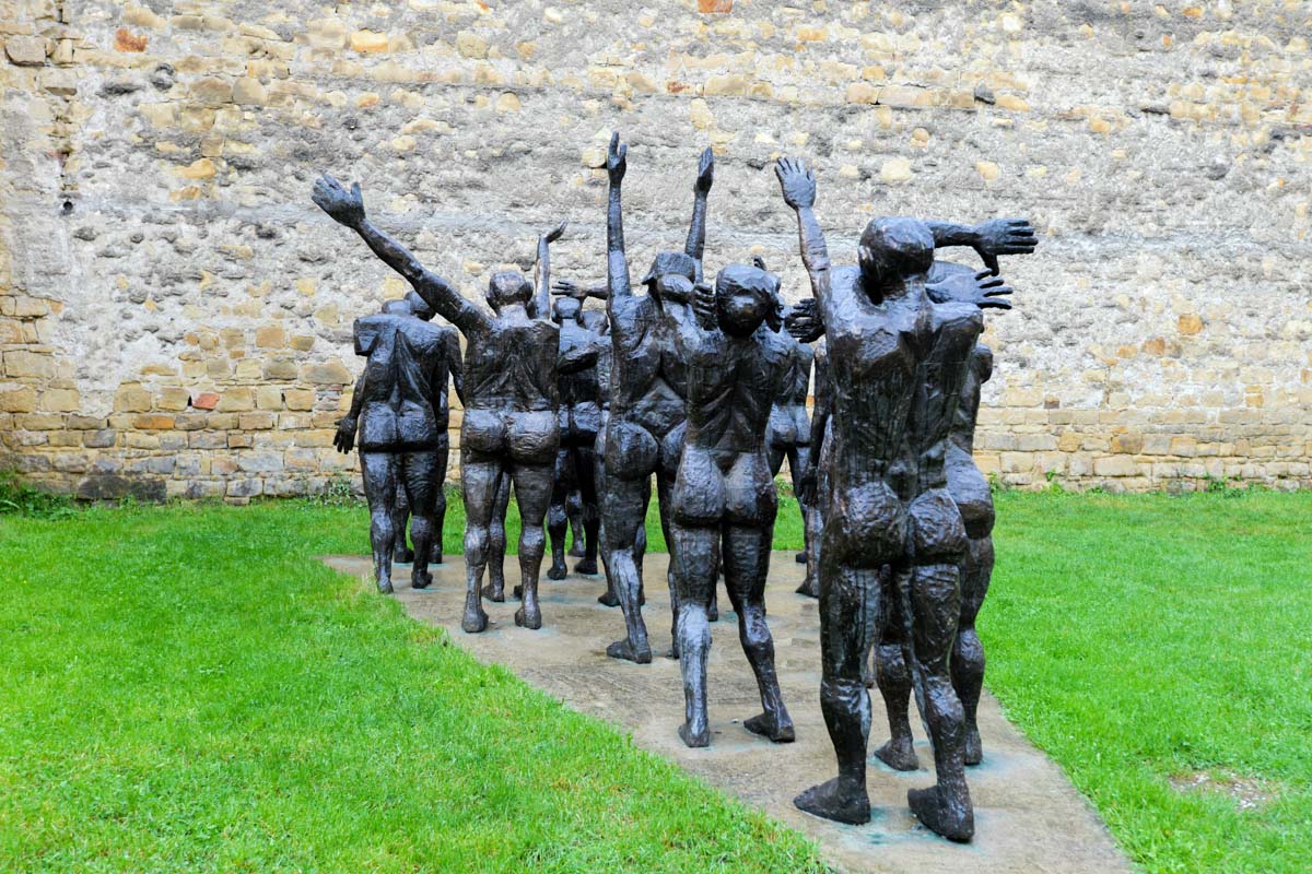 Die 18 Gestalten des Opferzugs im Sighet Memorial in Rumänien ziehen mit teils erhobenen Händen auf eine Mauer zu, die den Kommunismus symbolisiert